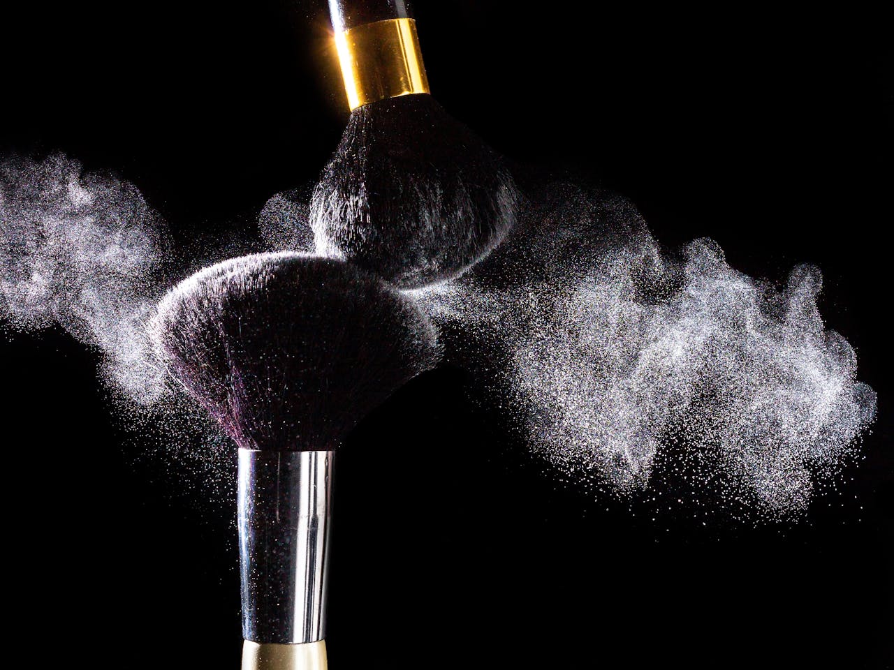 High-speed capture of makeup brushes dispersing powder against a black background.